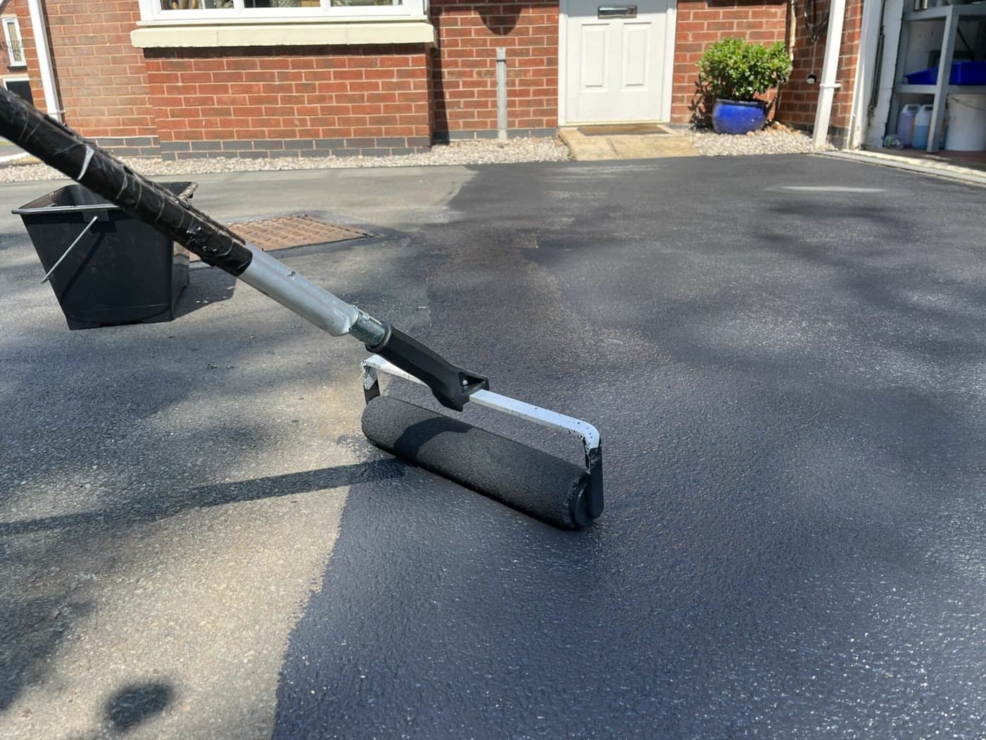 Hand rolling protective coating onto a driveway surface